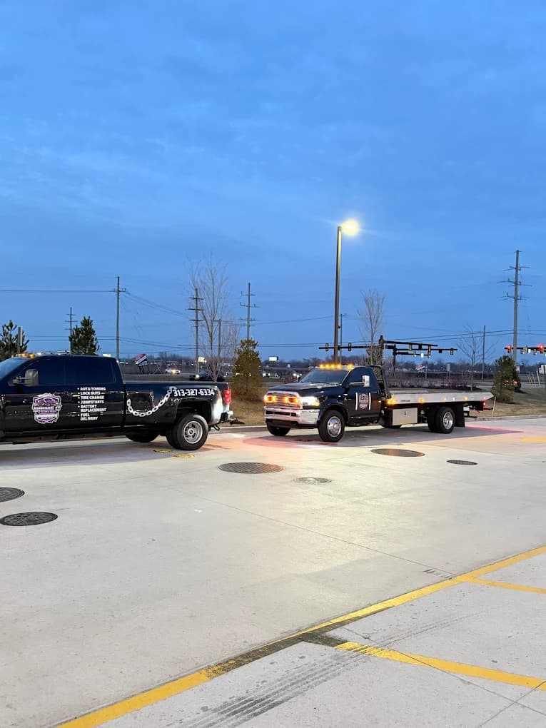 Prime O Towing wheel-lift Silverado and flatbed tow truck staged side by side at dusk in Metro Detroit