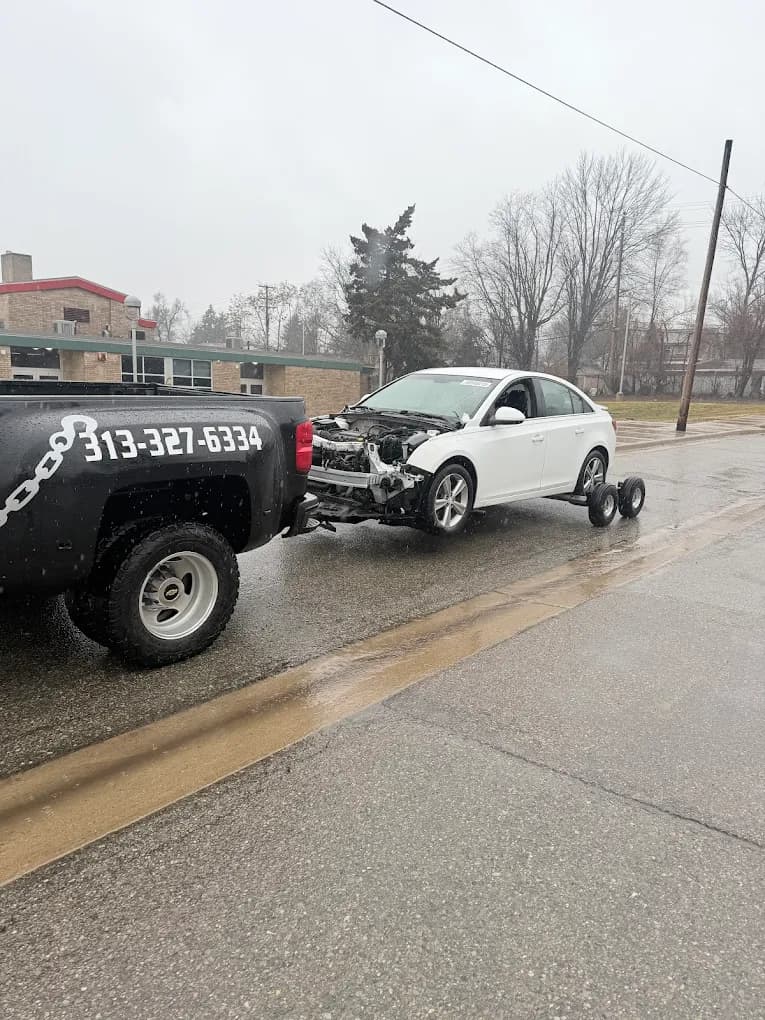 Prime O Towing wheel-lift Silverado towing a front-end damaged white Chevrolet Cruze from a Metro Detroit street
